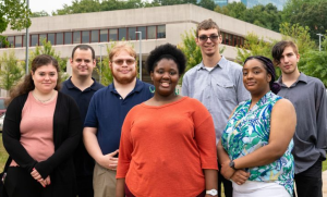 A group of 7 young people standing outdoors with a UConn hospital building in the background.