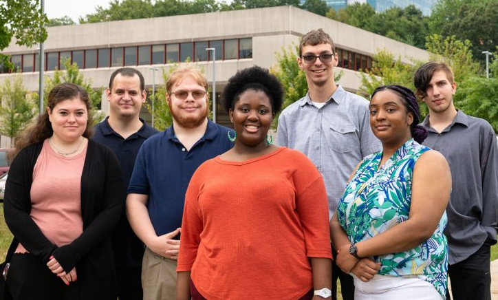 A group of 7 young people standing outdoors with a UConn hospital building in the background.