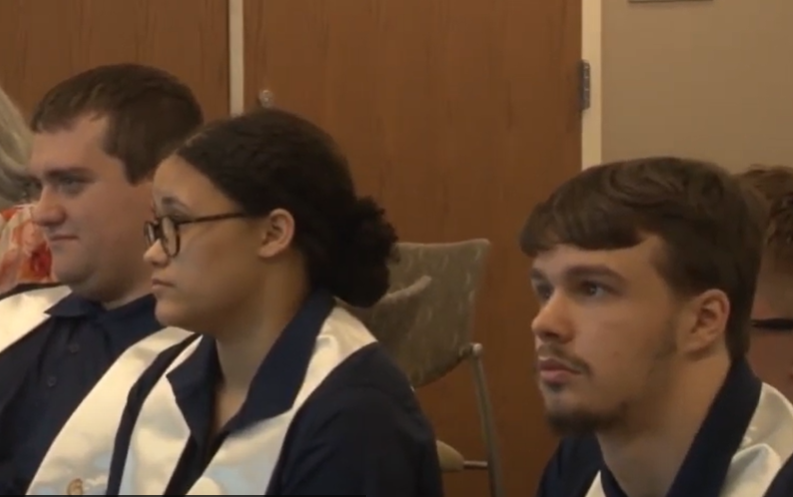 Close up of 3 young people in profile, at their graduation ceremony, listening to speakers.