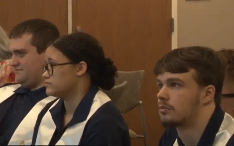 Close up of 3 young people in profile, at their graduation ceremony, listening to speakers.